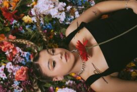 Caity Baser laying on lots of flowers, wearing a black top.